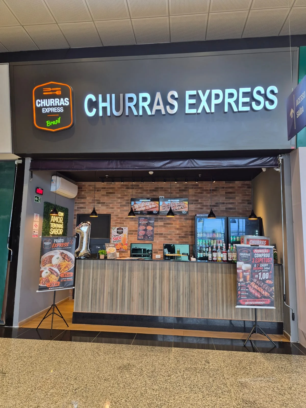 Fachada da loja Churras Express Guará, com o letreiro iluminado, na praça de alimentação do Shibata